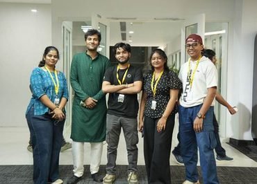 Group of five coworkers posing in a hallway, wearing yellow lanyards and smiling at the camera.