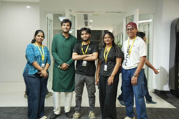 Group of five coworkers posing in a hallway, wearing yellow lanyards and smiling at the camera.